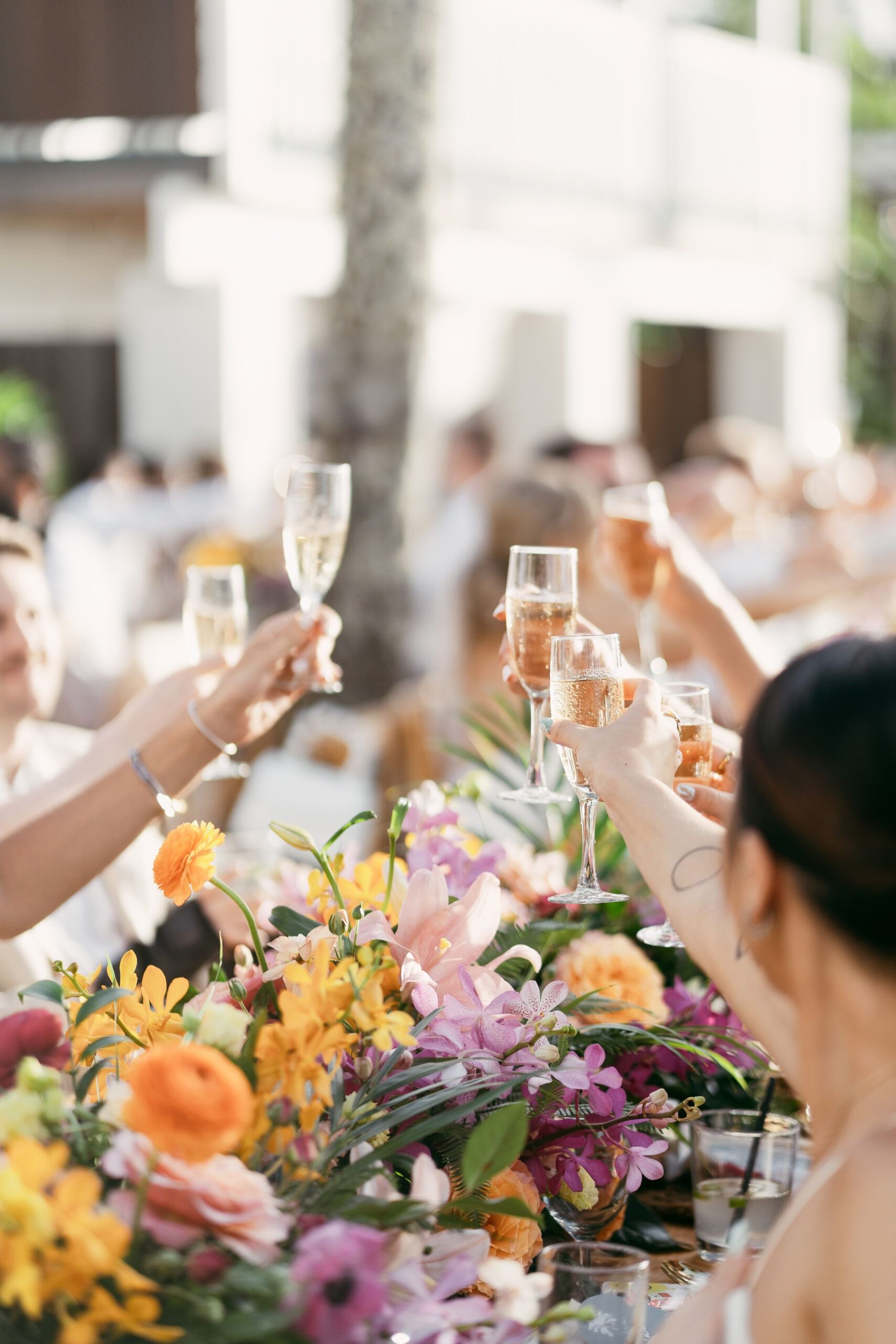 People toasting with champagne glasses over a vibrant floral centerpiece at a tropical celebration.
