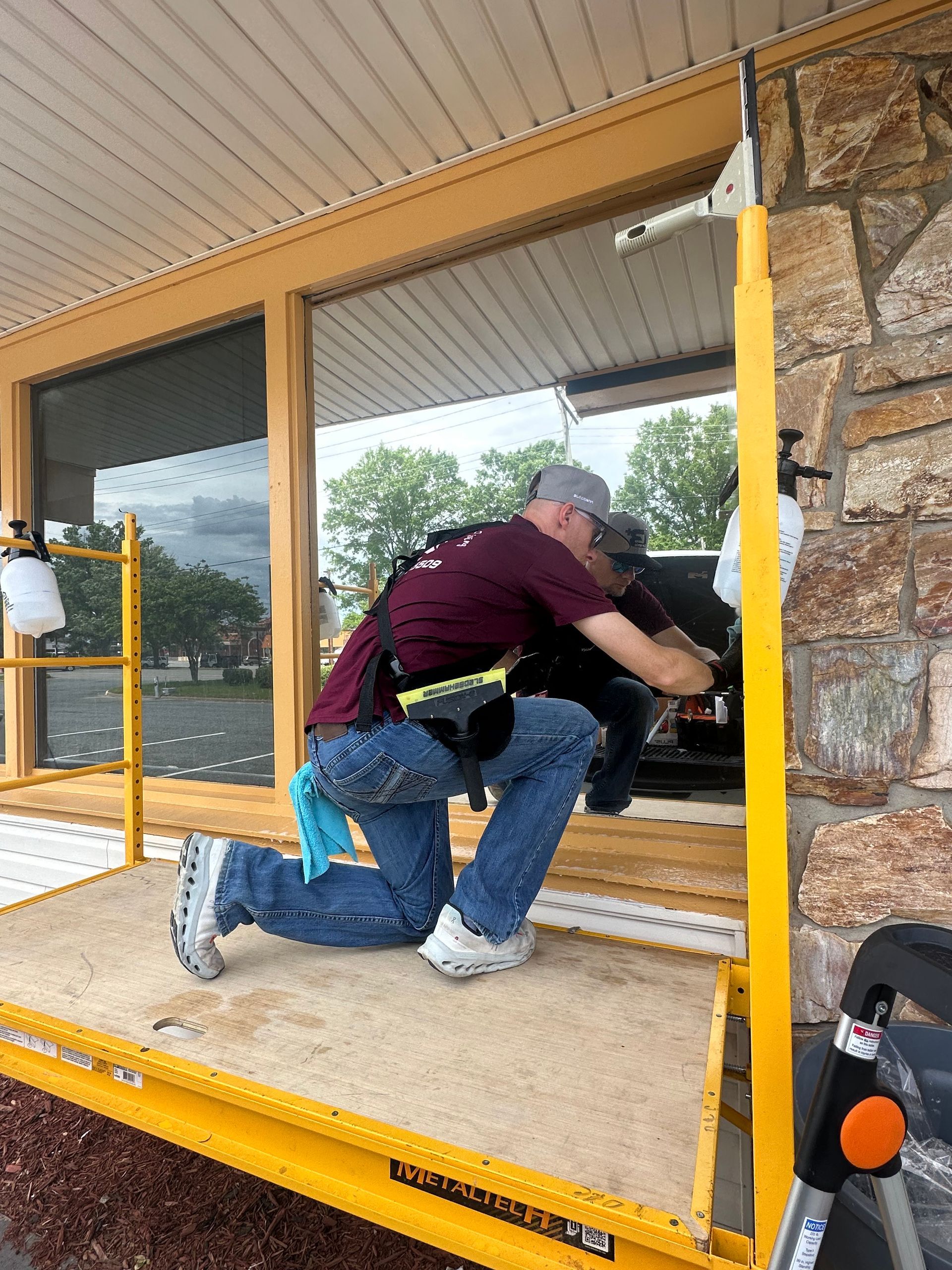 A man is kneeling on a scaffolding working on a window.