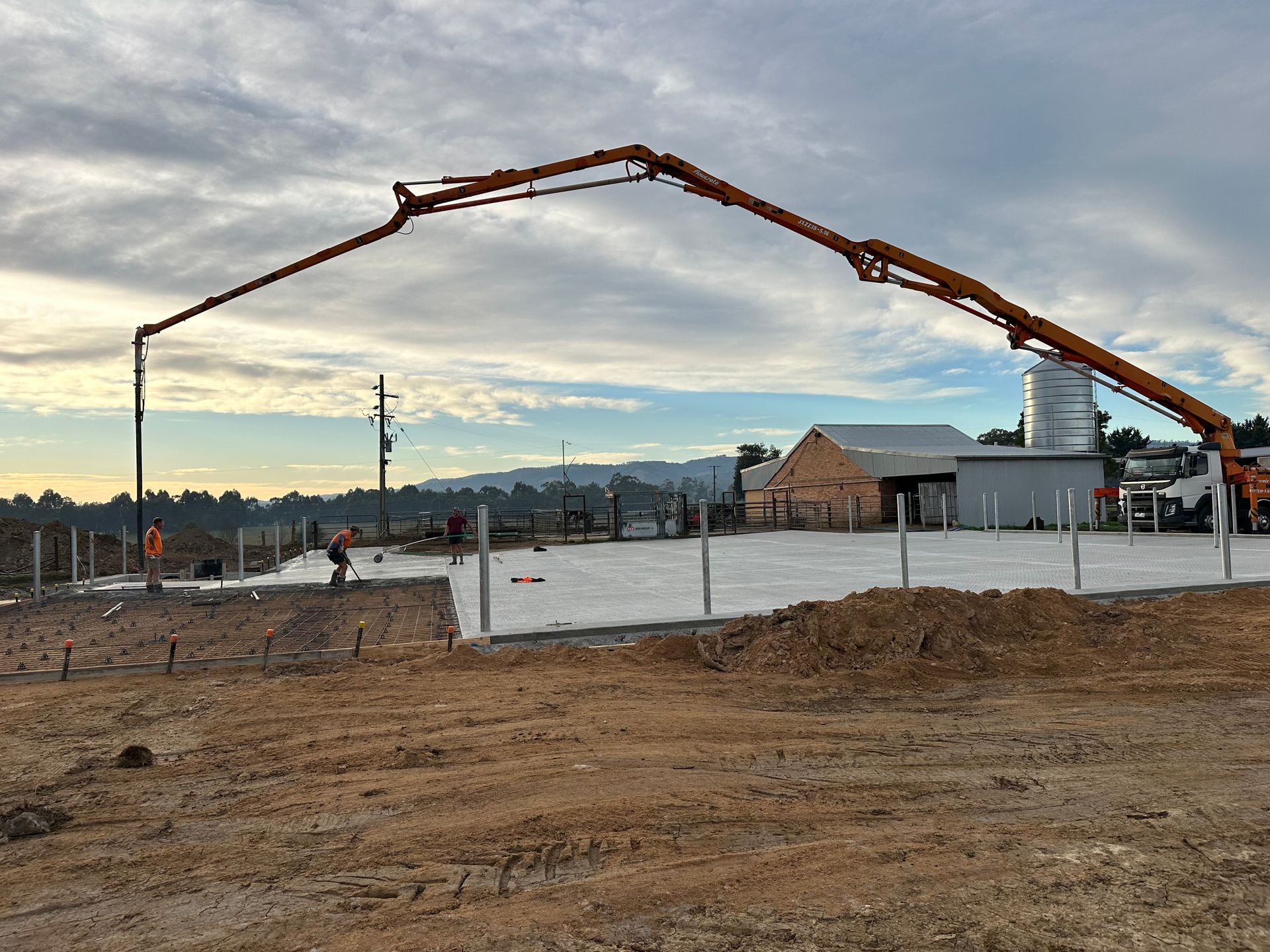 A concrete pump is being used to pour concrete into a dirt field.