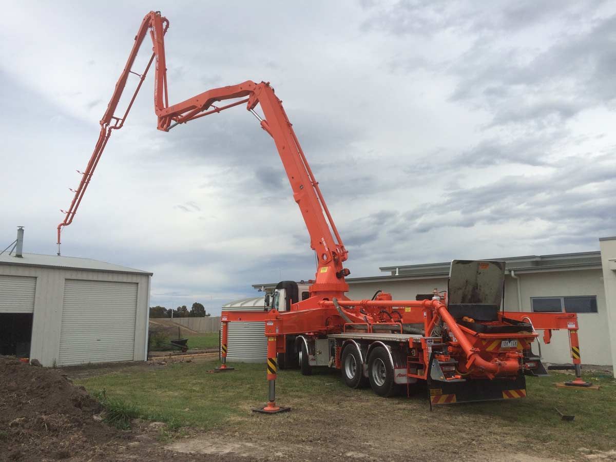 A large orange concrete pump is sitting in front of a building.