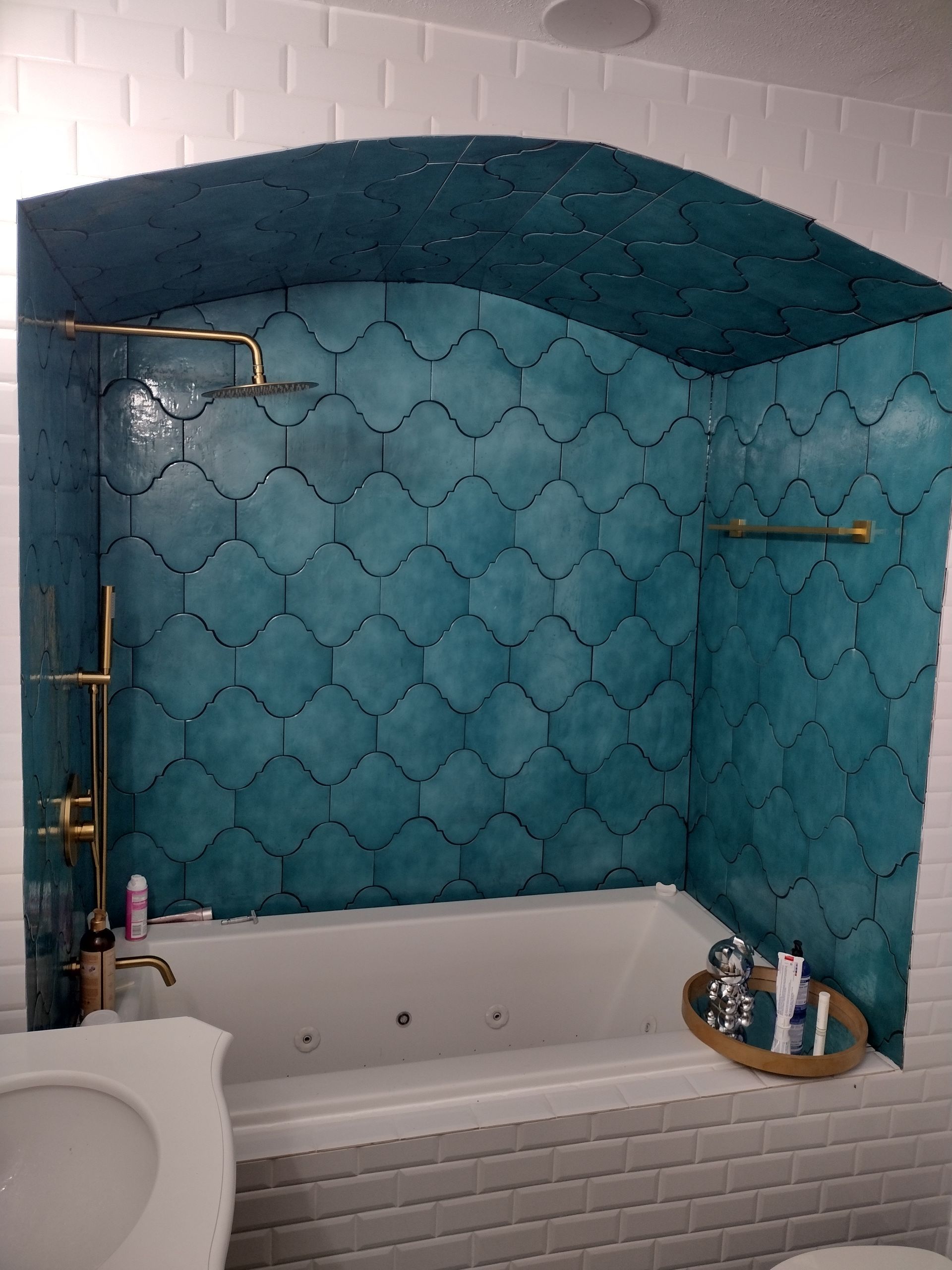 Bathroom with a turquoise tiled shower alcove over a white bathtub. Brass fixtures and white subway tile.