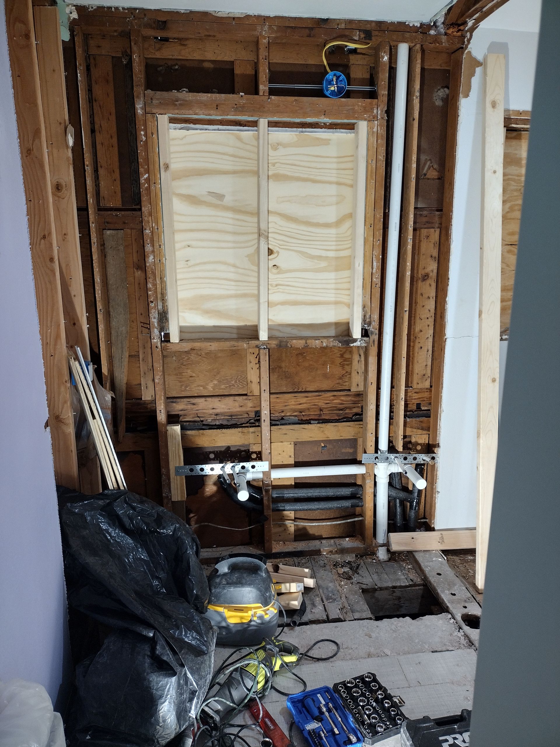 Bathroom remodel in progress; exposed studs, plumbing, electrical box, wooden framed niche with plywood backing. 