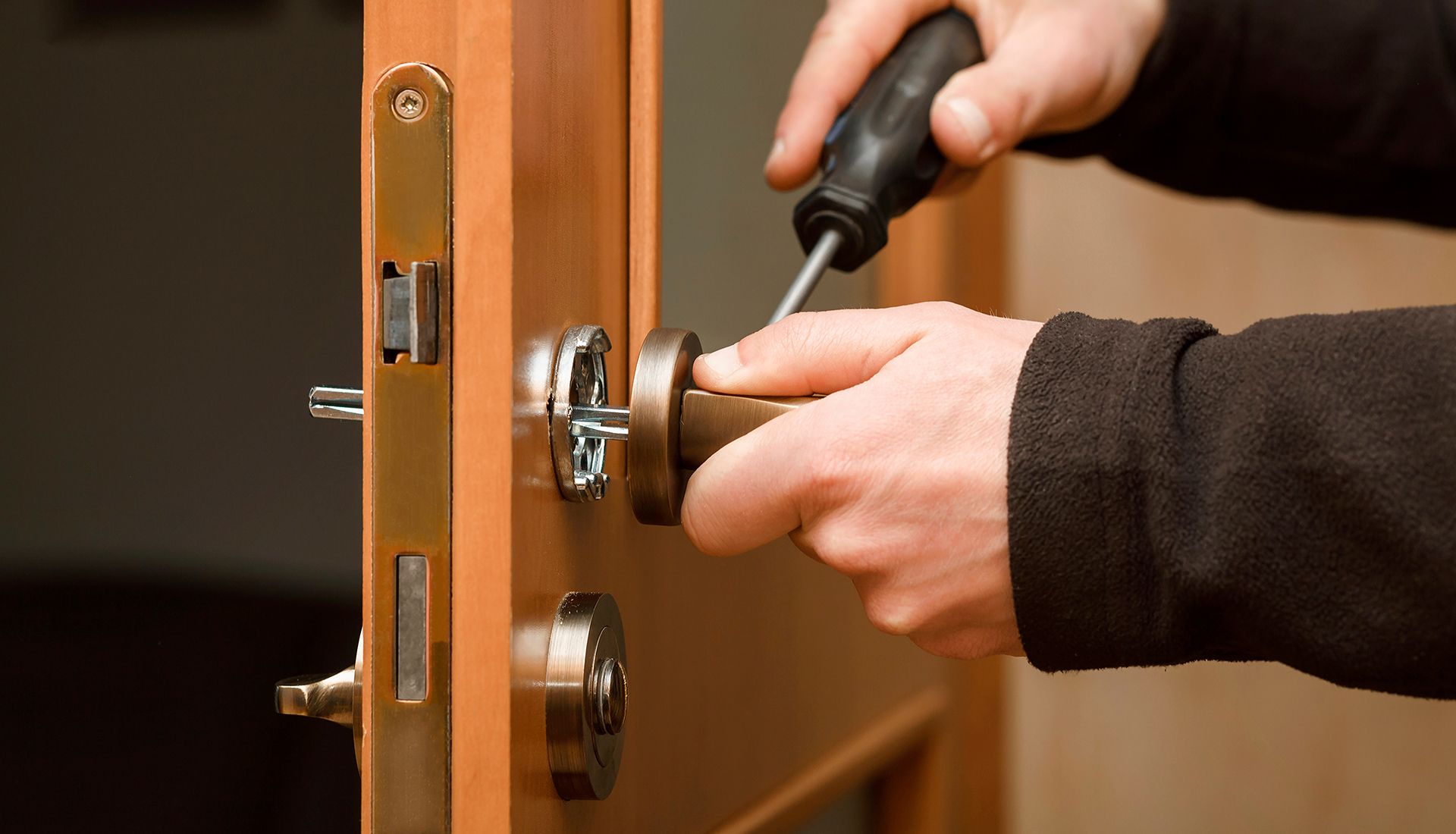 Person using a screwdriver to install a door handle on a wooden door.