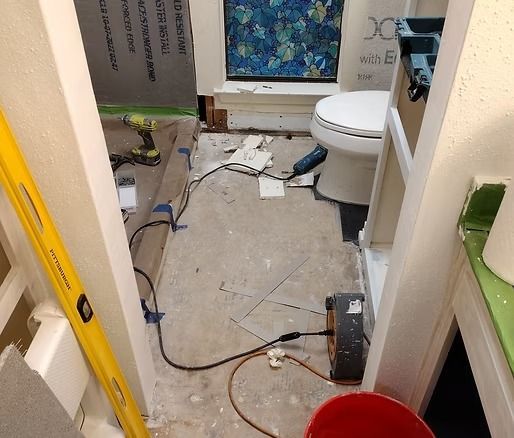 Bathroom under renovation; exposed floor, tools, toilet, and shower area visible.