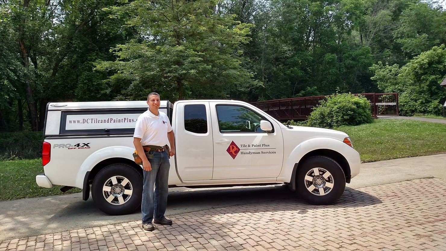 Man standing next to a white pickup truck with company logo. Outdoors, trees in the background.