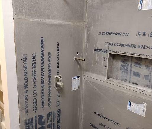 Gray shower wall with installed cement board, plumbing fixtures, and a recessed shelf.