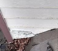 Damaged white siding and roof edge with fallen leaves. Pink wood beam in corner.