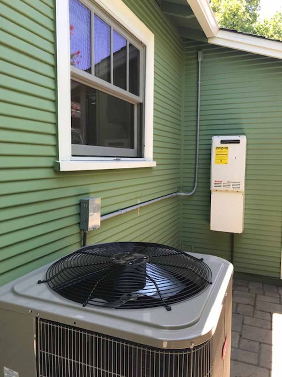 An air conditioner is sitting on the side of a green house next to a window.