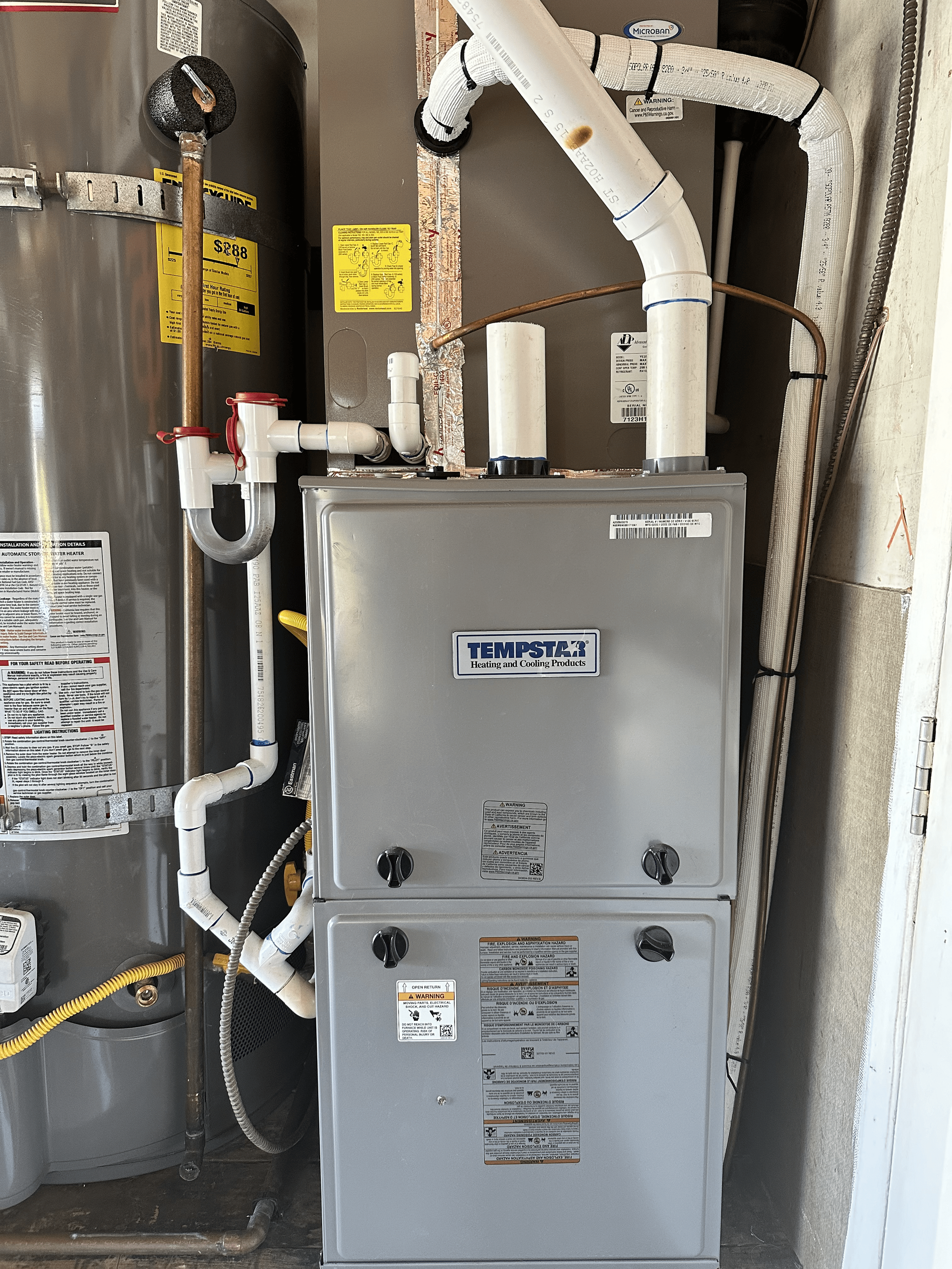 A gray furnace is sitting on a wall next to a water heater.
