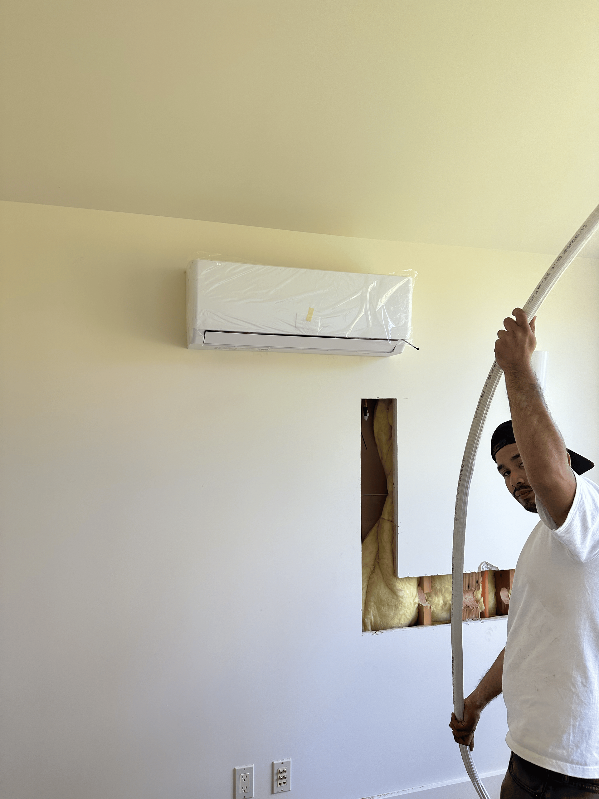 A man is holding a hose in front of a wall.