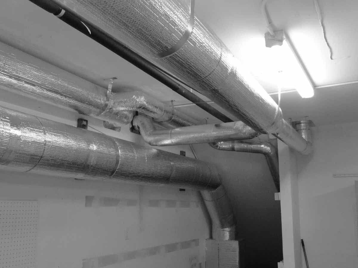 A black and white photo of a room with pipes and a light.