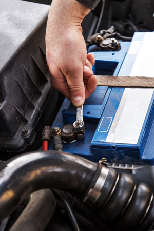 A person is fixing a car battery with a wrench.