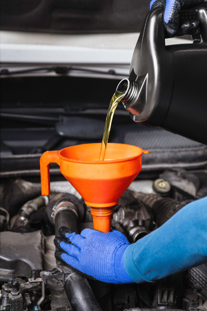 A person is pouring oil into a car through a funnel.