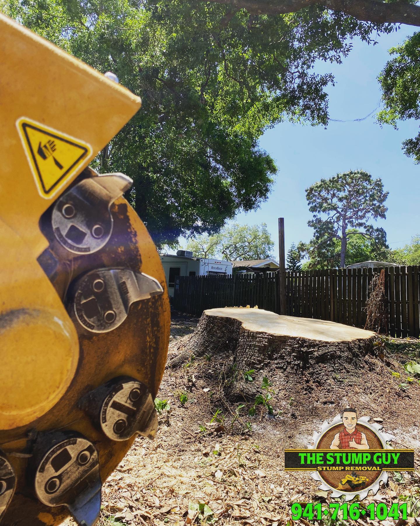 Yellow stump grinder next to a tree stump in a yard on a sunny day.