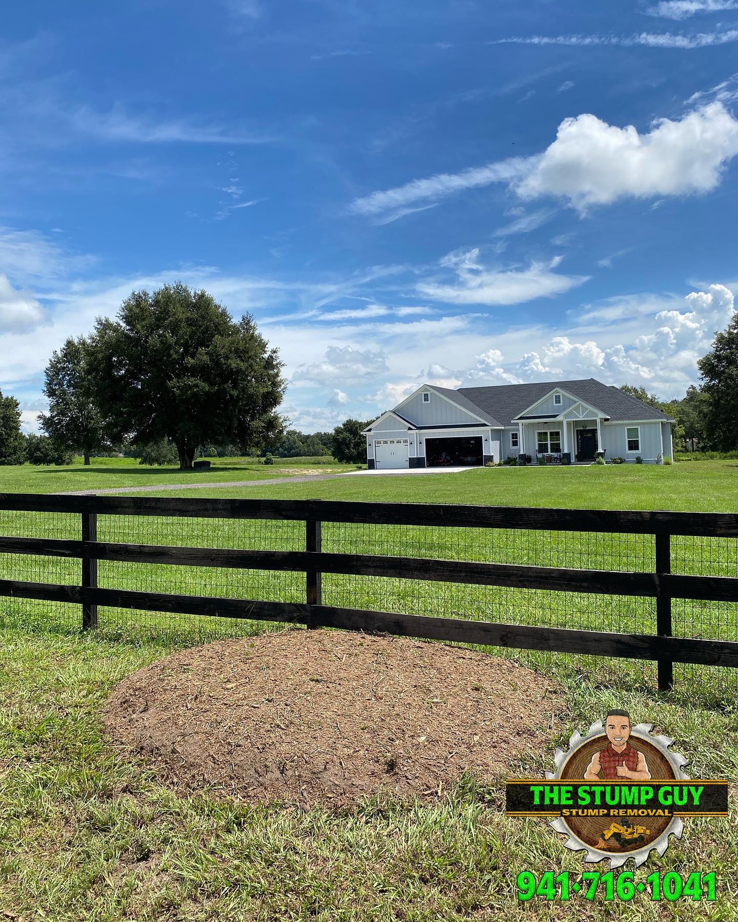 Large yard with a house, fence, and tree. A stump pile is in the foreground. Blue sky with clouds.