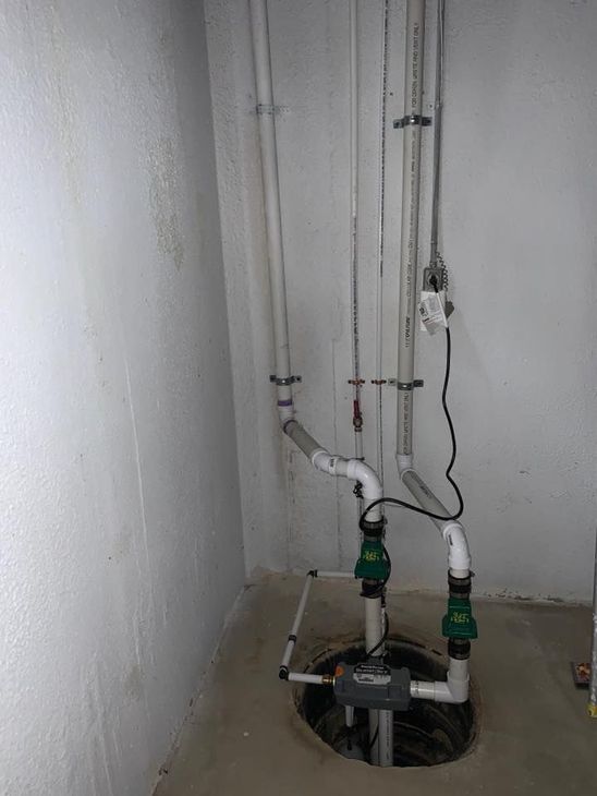 A basement with a sump pump and pipes coming out of it.