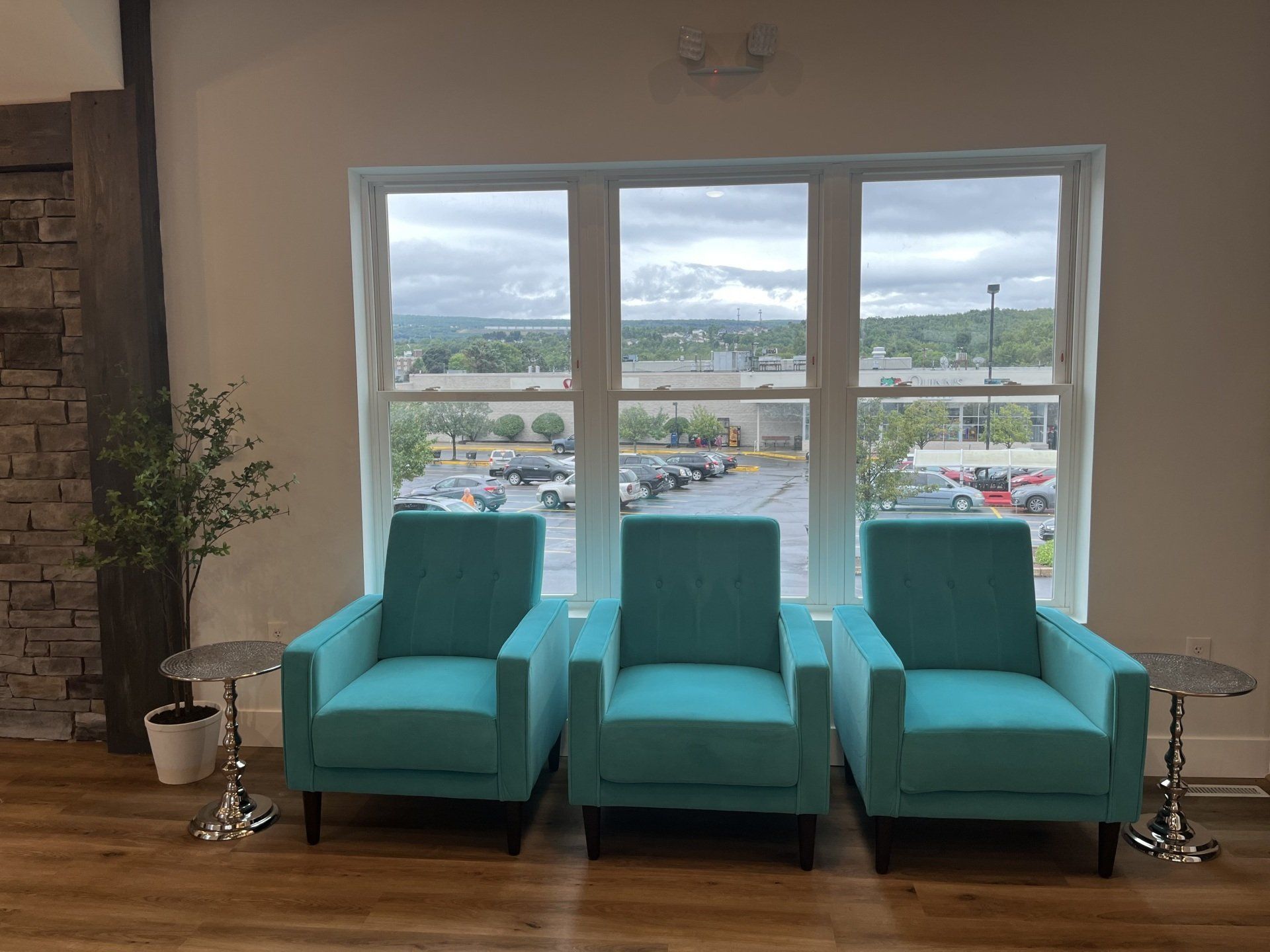 Three blue chairs are sitting in front of a window in a waiting room.