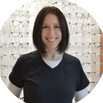 A woman is smiling in front of a wall of glasses.