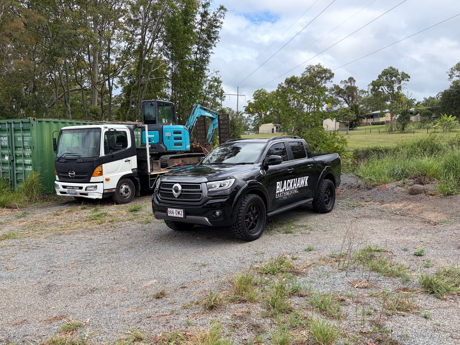 An excavator places a gray block onto a retaining wall being built in a wooded area.