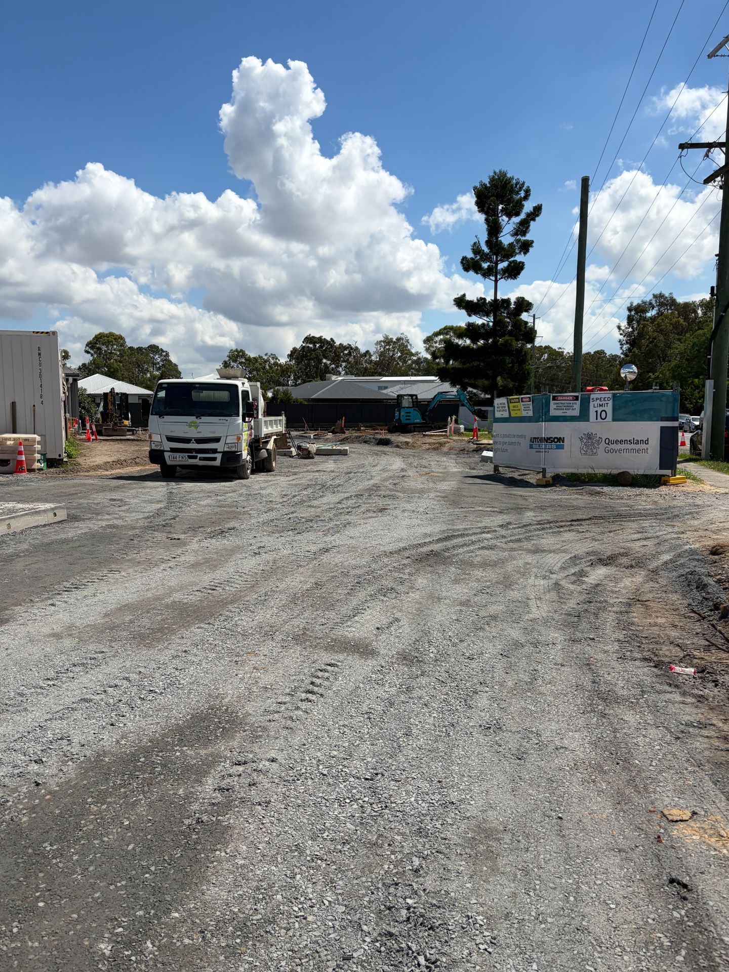 Blue excavator digging in a construction site with dirt and concrete blocks under a blue sky.