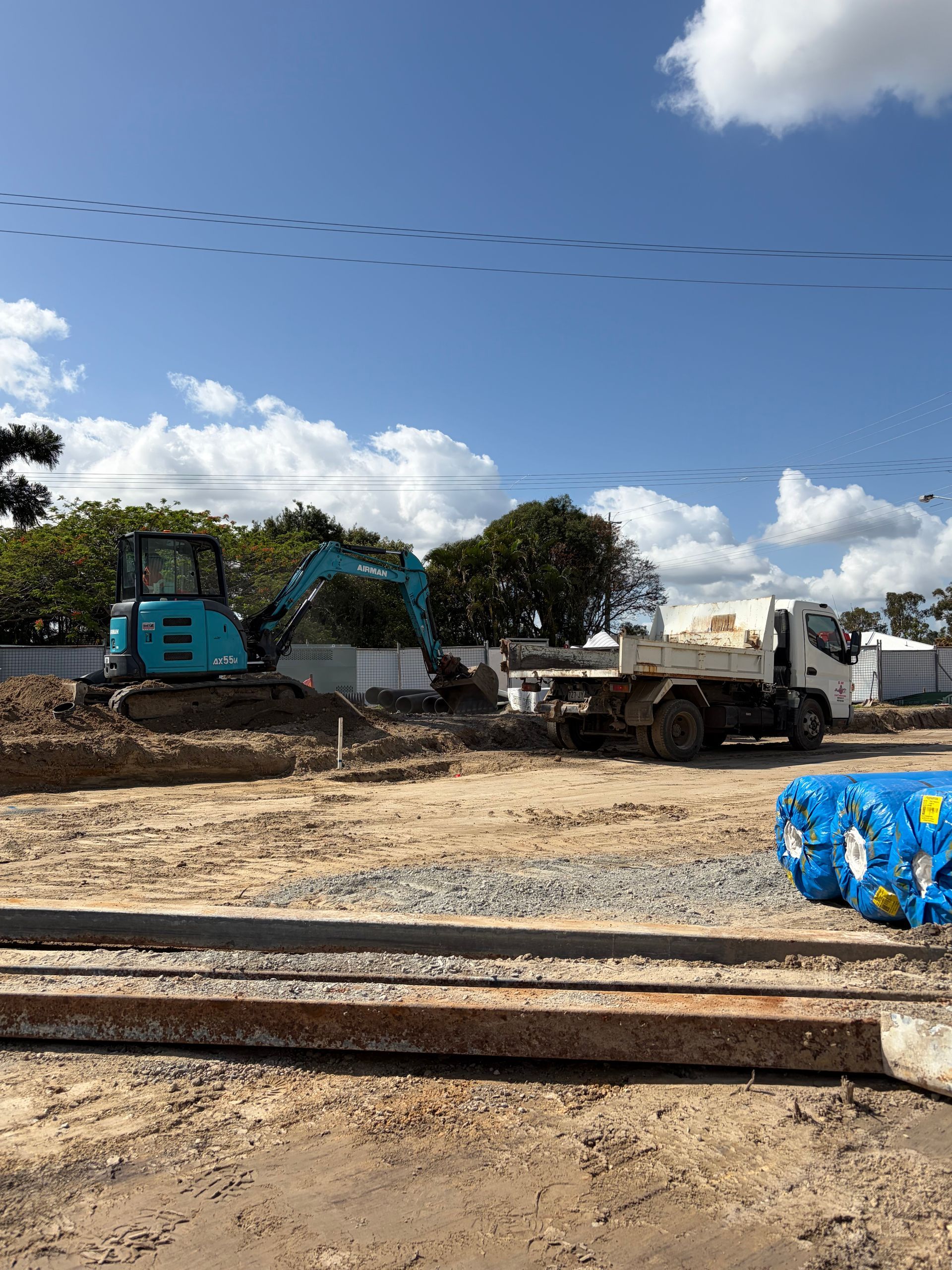 Construction site: Blue excavator, dump truck, sunny sky with clouds and bird trail.