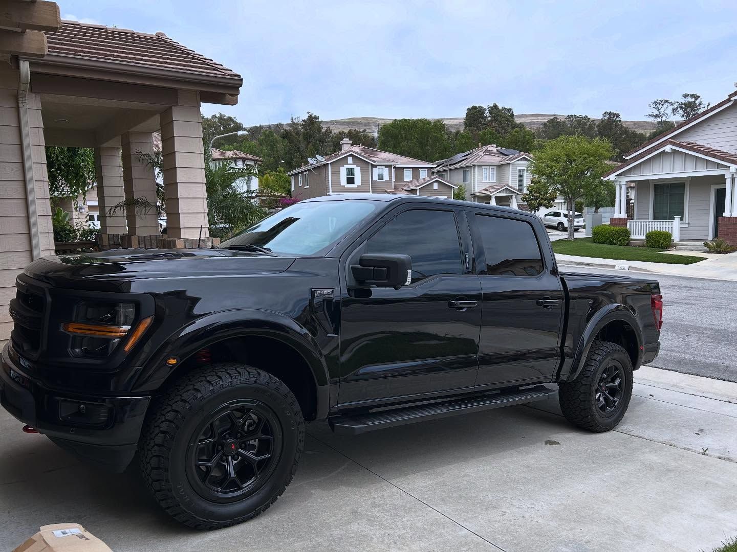 Black Ford pickup truck parked on a driveway in a residential neighborhood.