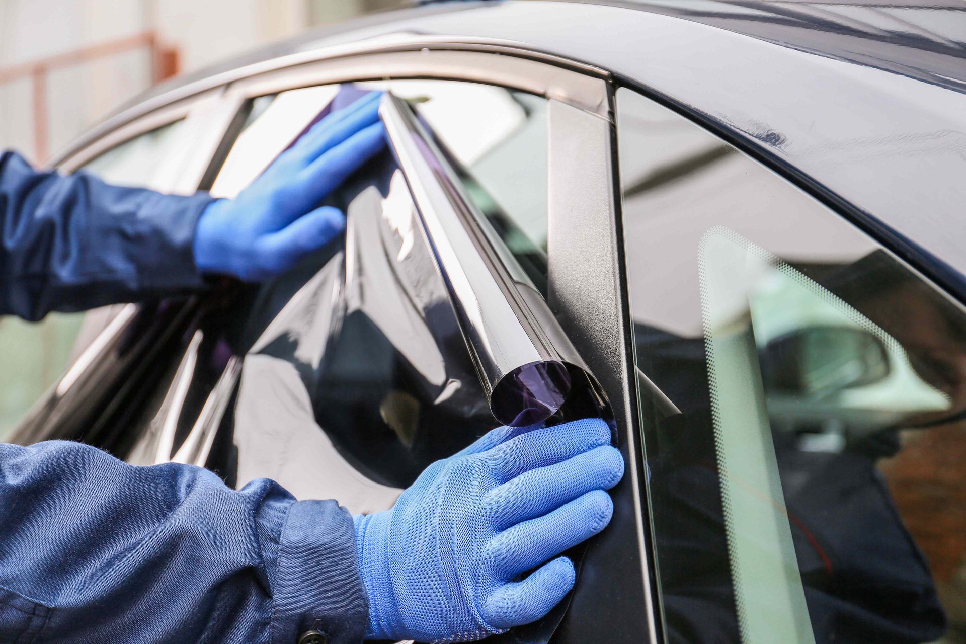 Hands in blue gloves applying tinted film to a car window.