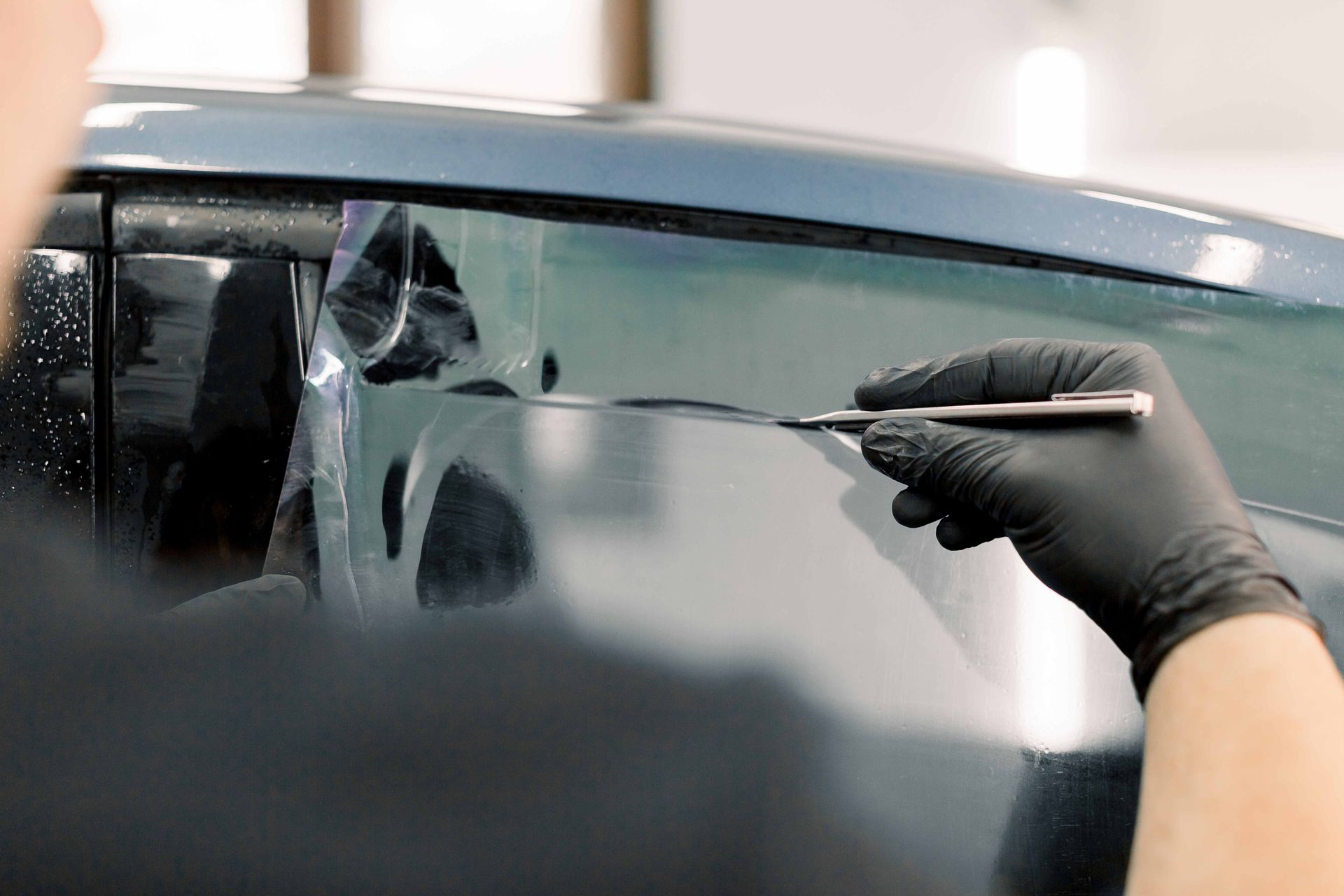 Person with black gloves using a blade to trim window tint on a car.