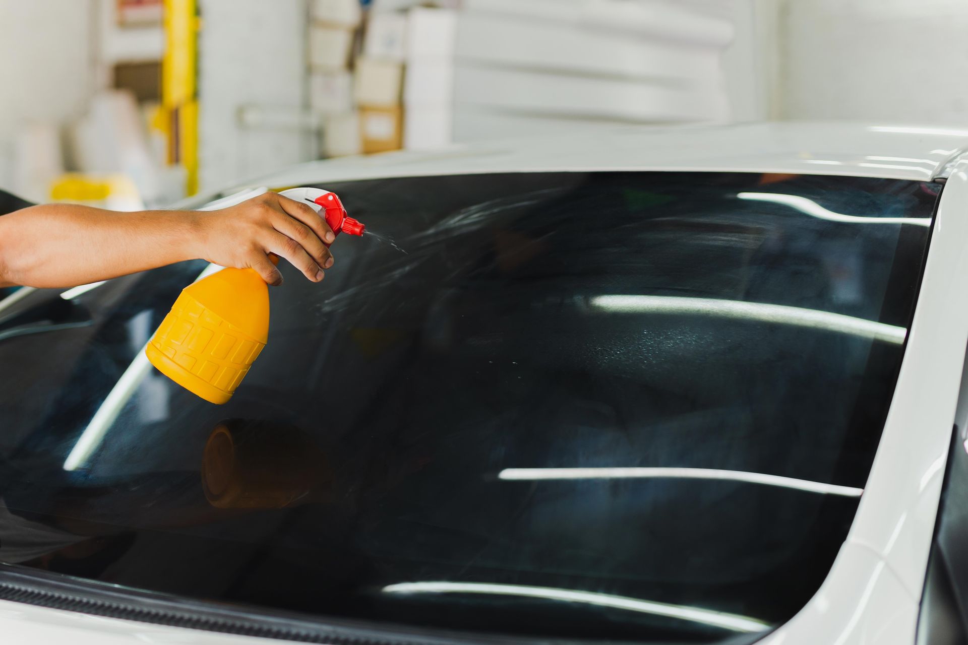 Person sprays liquid on a car's tinted windshield inside a shop.