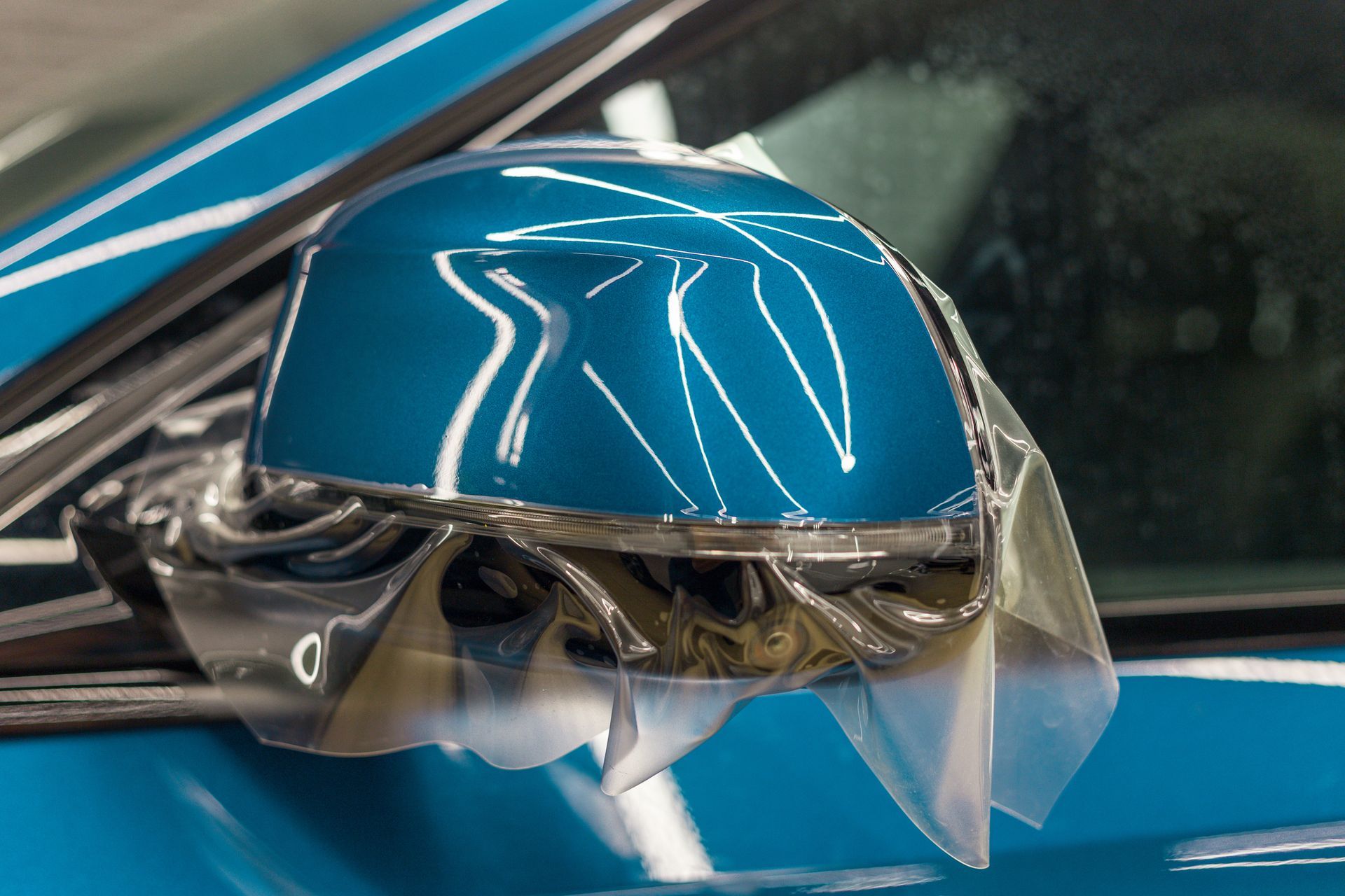 Person polishing a dark car hood with a blue buffer, lit by overhead lights.
