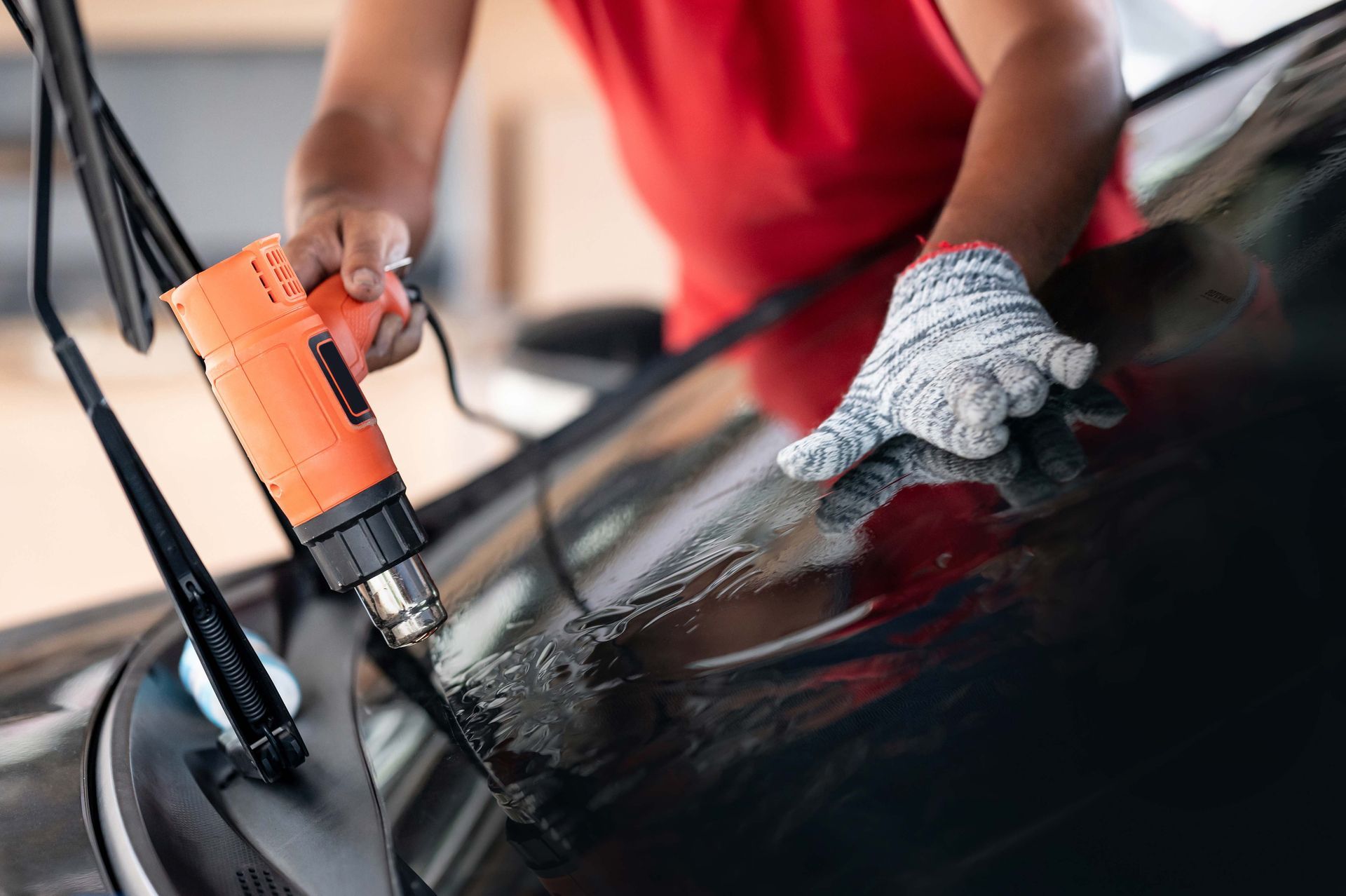 Person using a heat gun to apply tint film to a car windshield.