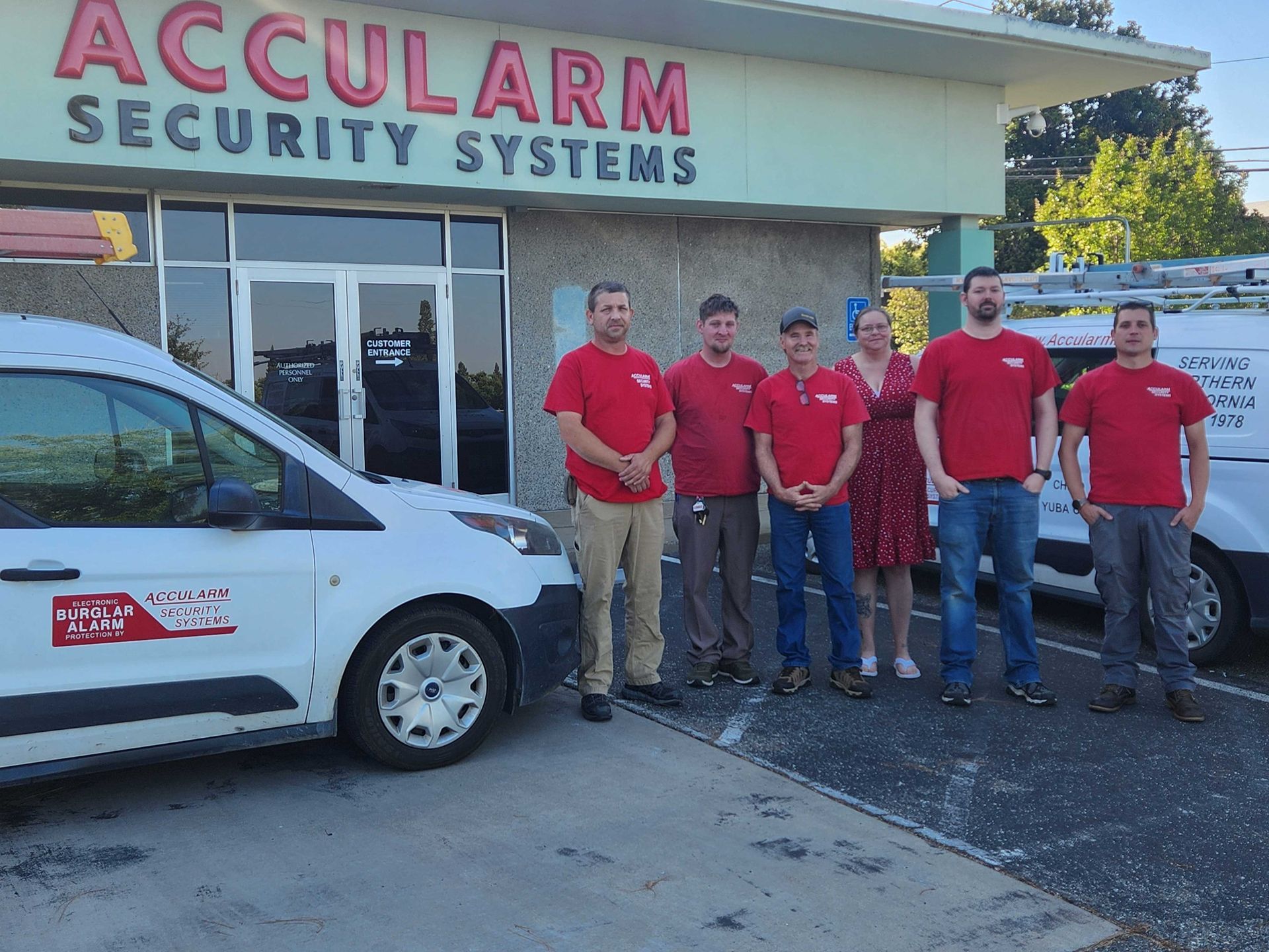 Accularm Security Systems staff pose outside their business. They wear red shirts, stand beside vans.