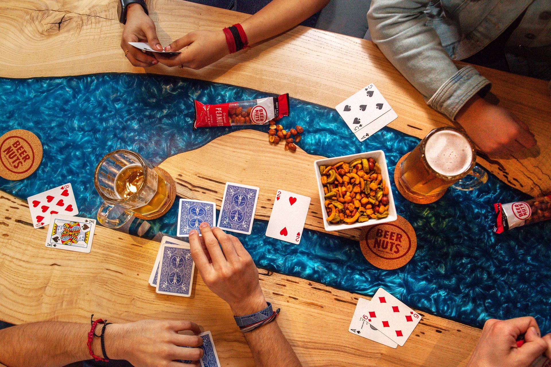 Overhead view of people playing cards with beer and snacks on the table
