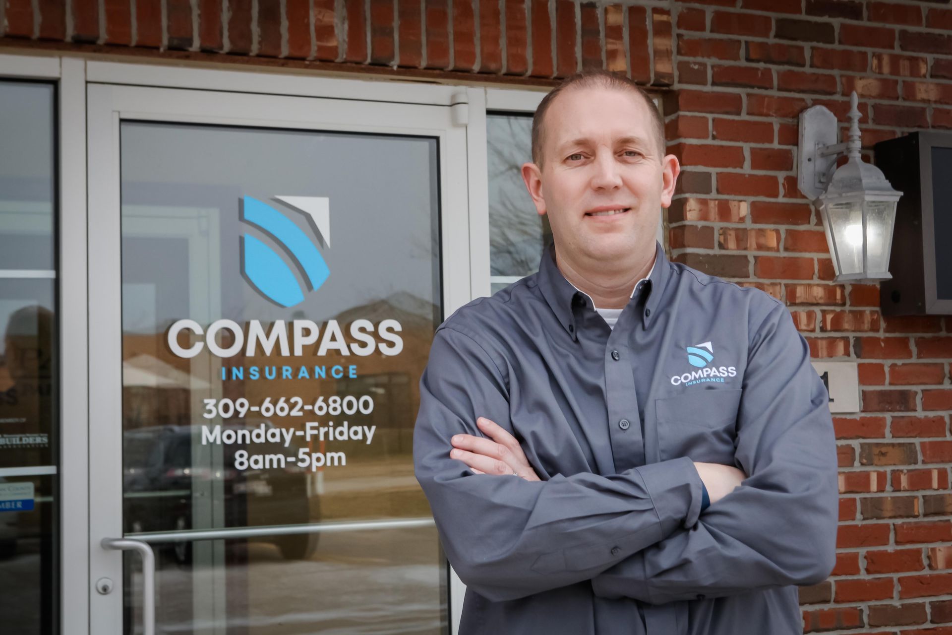 man standing with his arms crossed in front of his business door