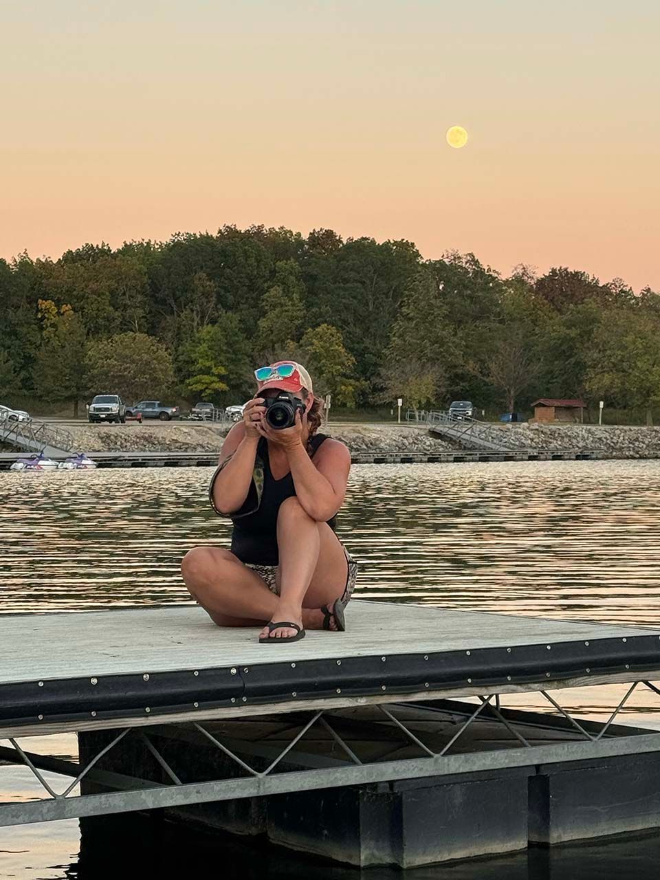 Woman photographing sitting on a dock with the moon in the background