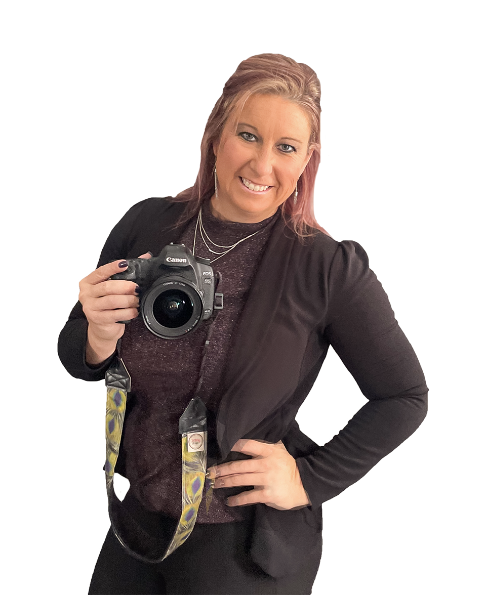 Woman in black blazer and purple shirt, holding a camera, smiling.