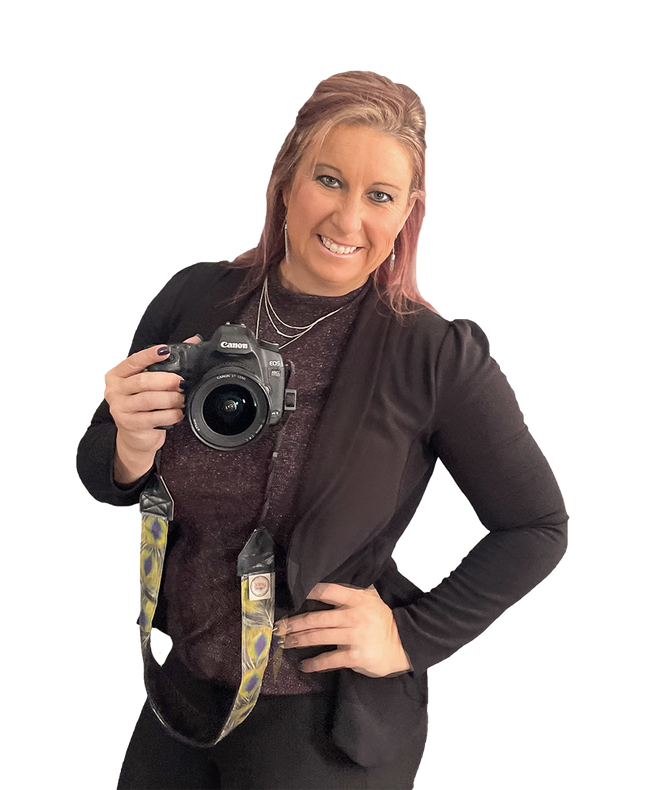 Woman in black blazer and purple shirt, holding a camera, smiling.