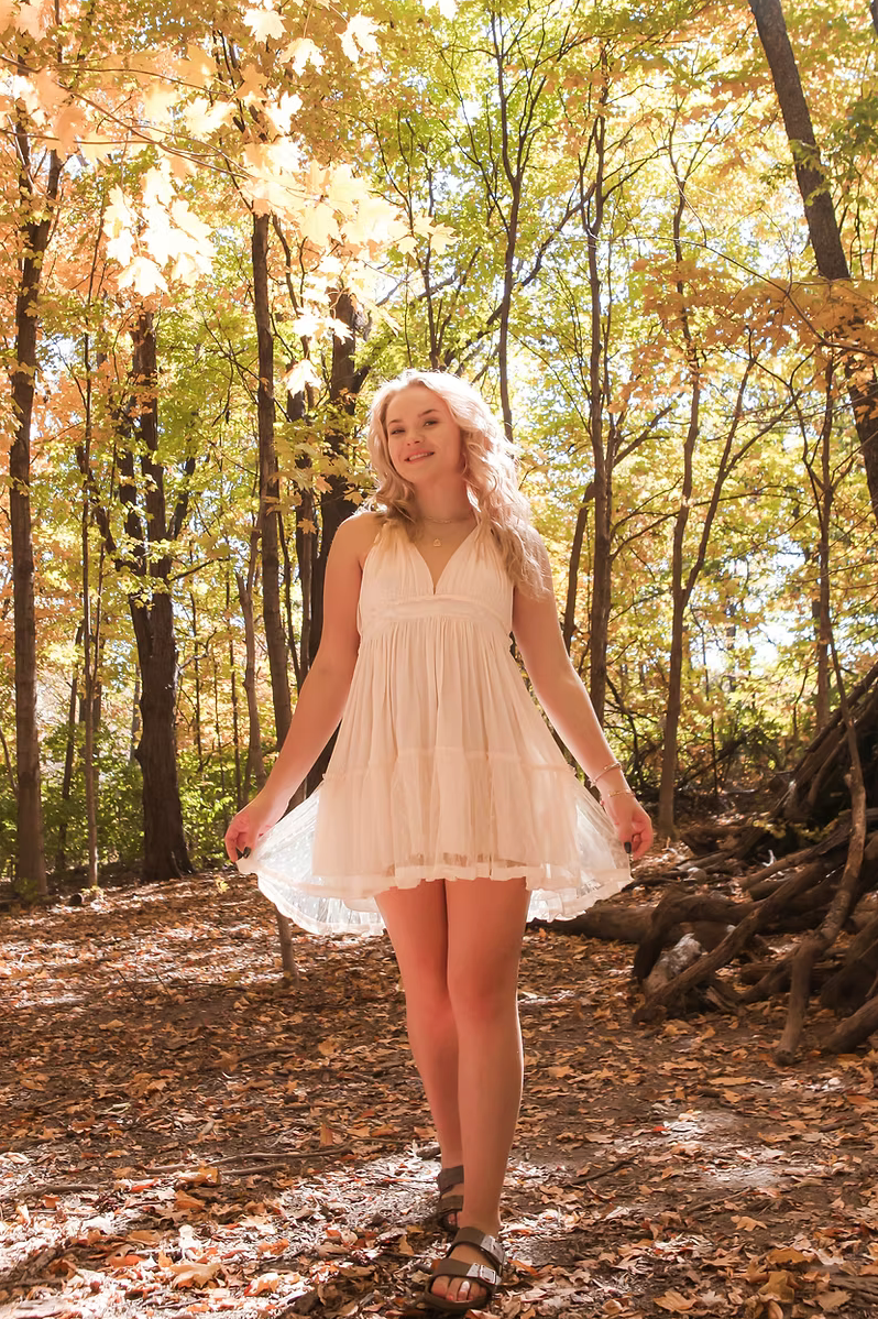 senior girl with white dress in the woods backlit by the sun