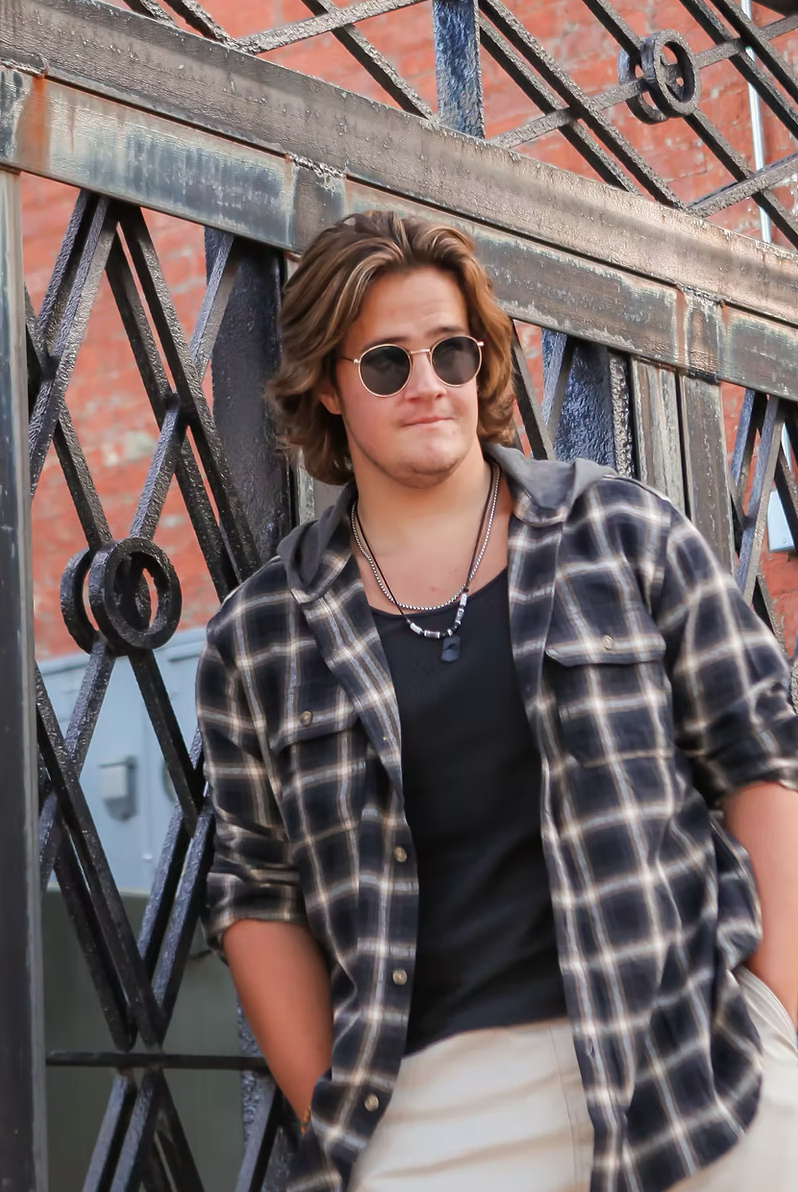 senior boy looking cool by a gate in sunglasses