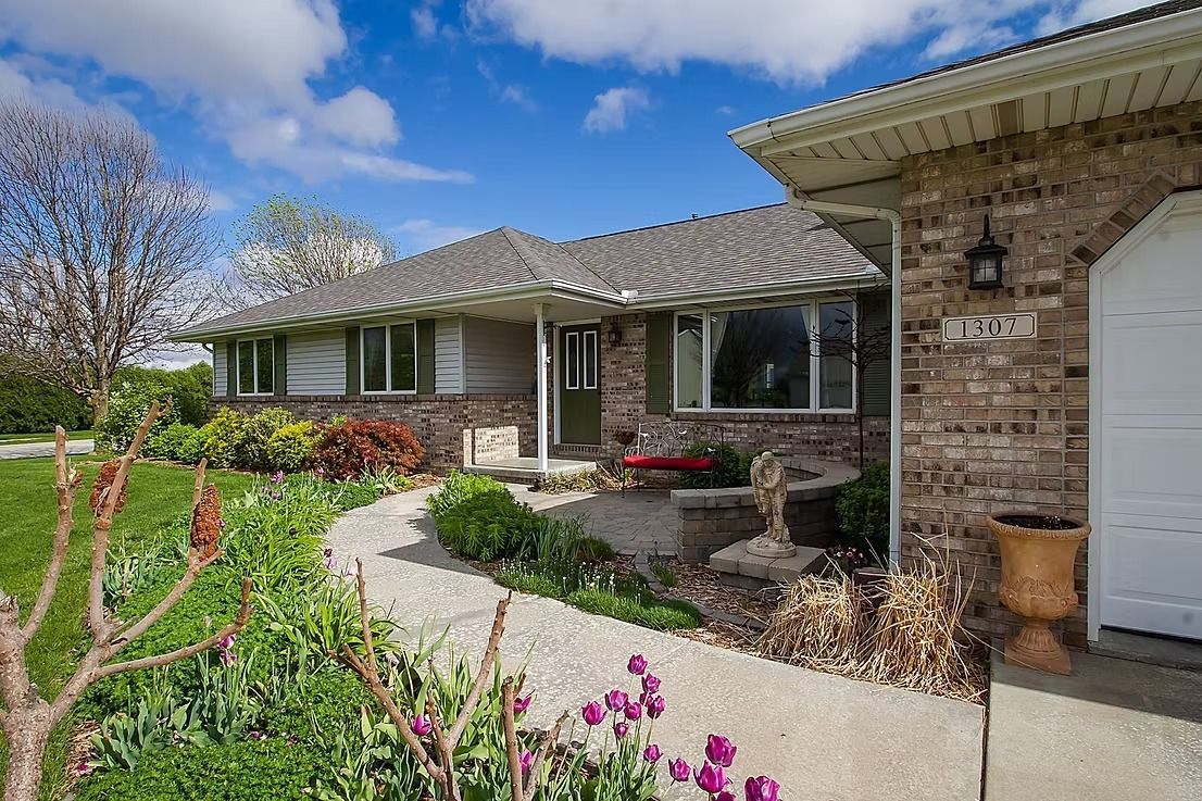 Brick ranch home with a curved walkway, lush garden, and blue sky.