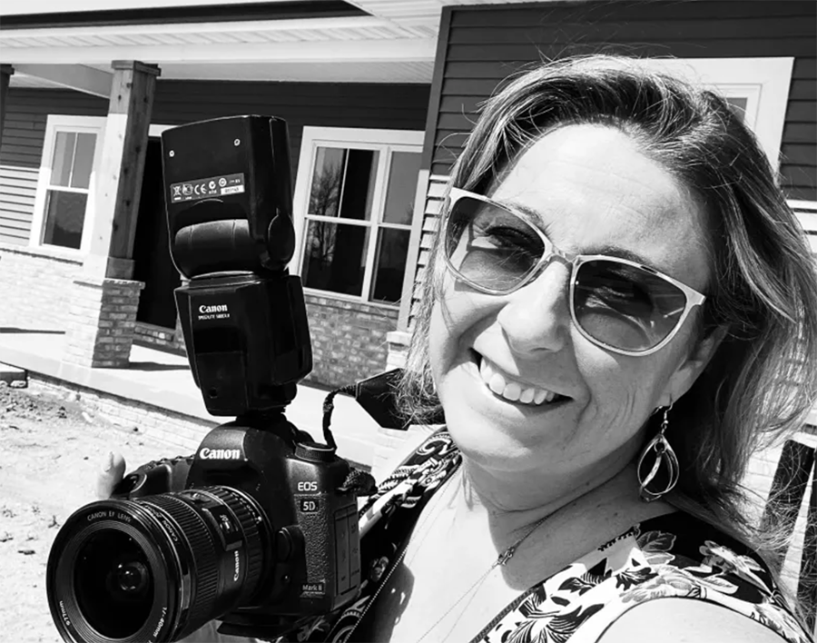 photographer smiling with camera in front of a house