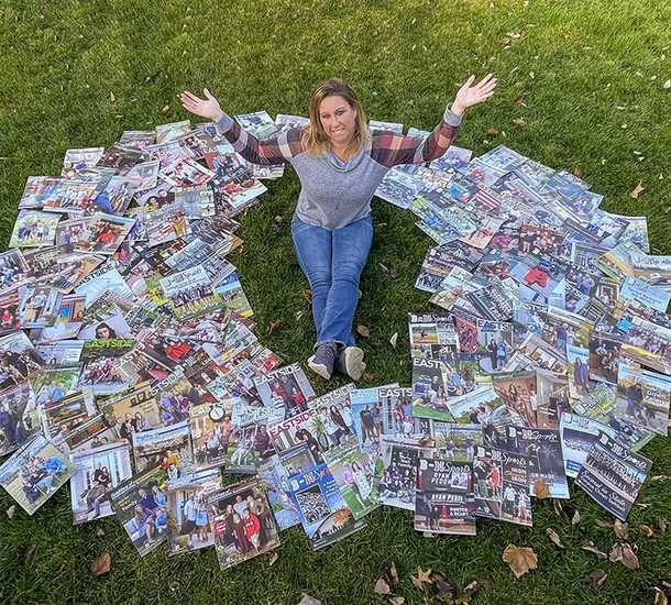 Woman sitting inside a circle of completed jigsaw puzzles on grass, arms raised.