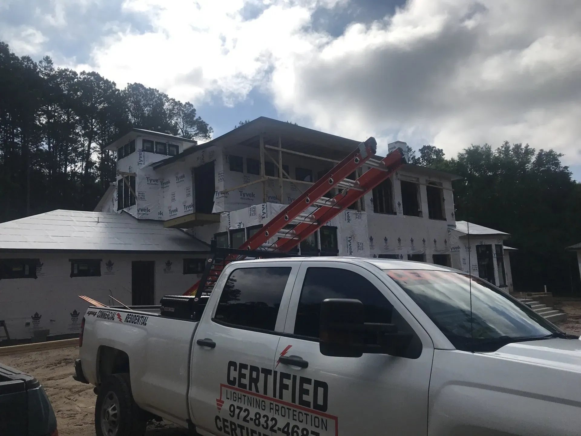 A certified construction truck is parked in front of a house under construction.