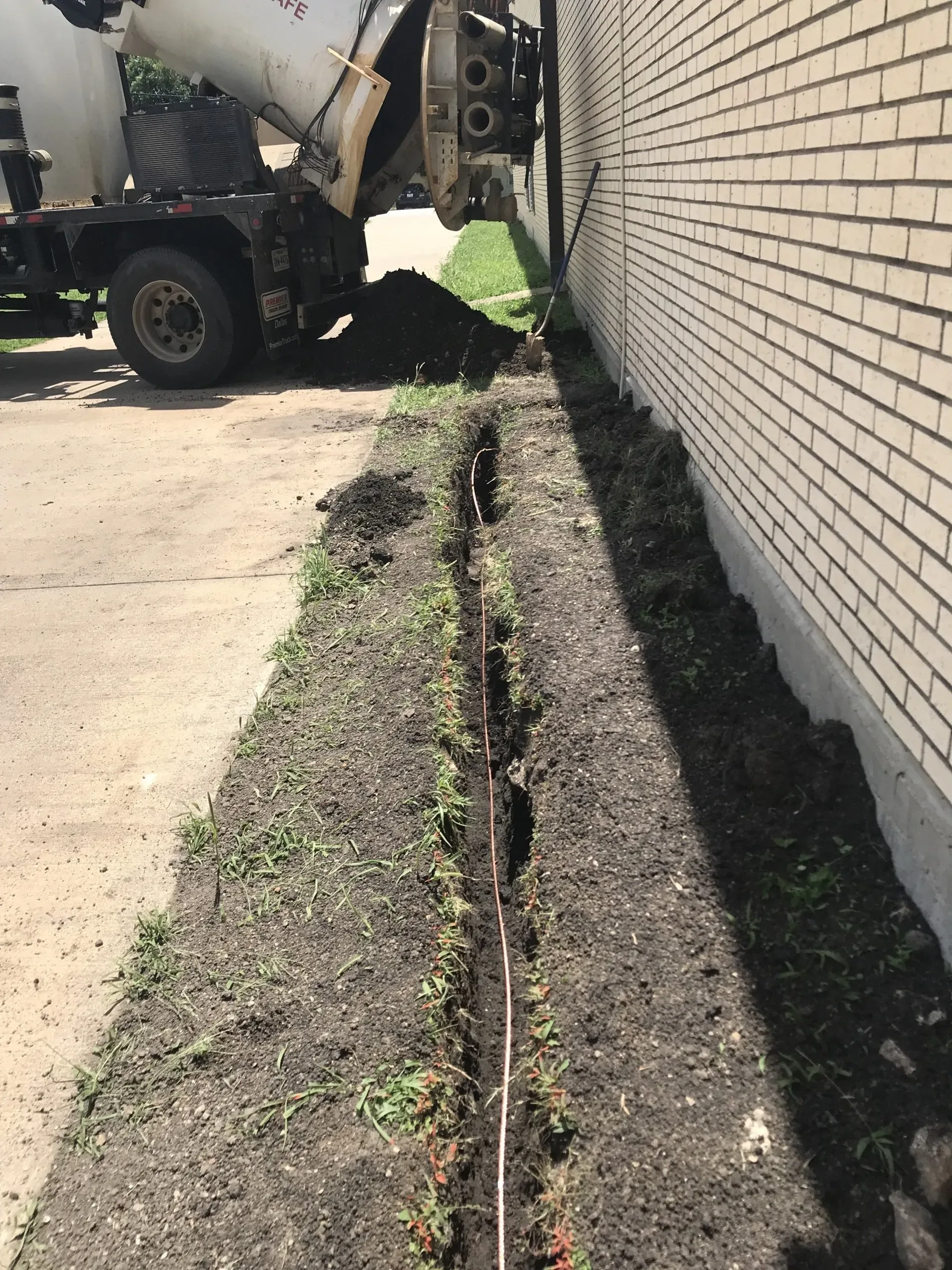 A cement truck is pouring concrete into a trench next to a brick wall.