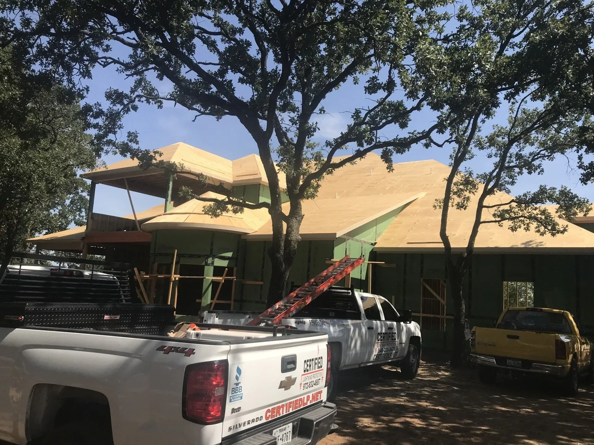 Two trucks are parked in front of a house under construction.