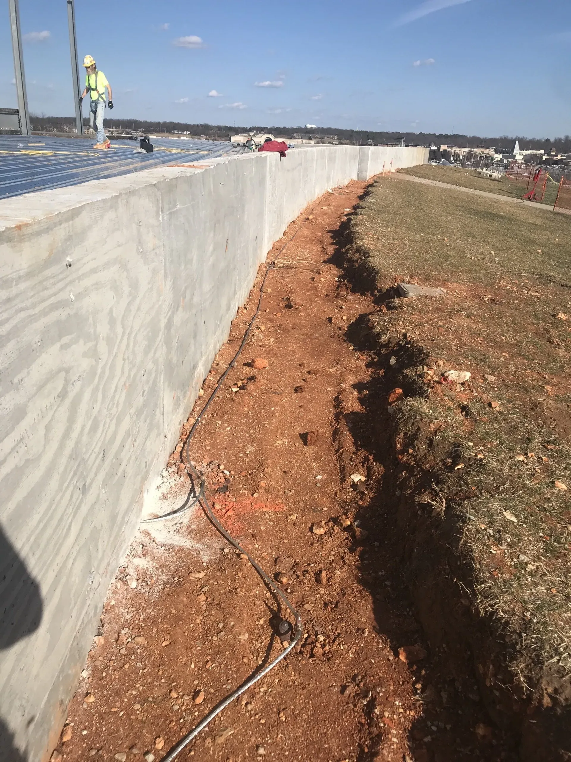 A construction worker is standing on top of a concrete wall.