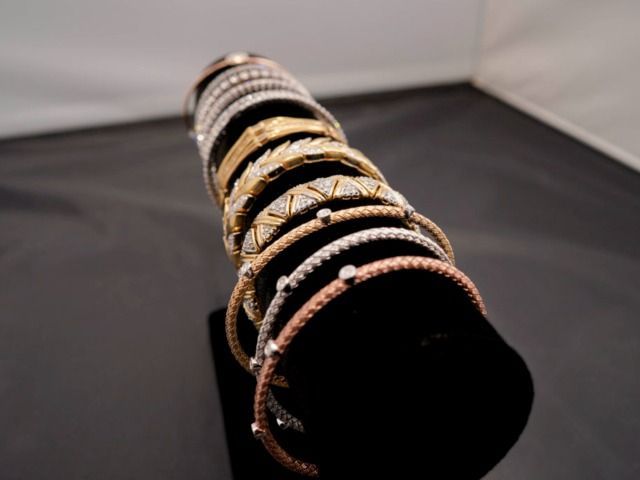 A stack of metallic and jeweled bracelets arranged in a row on a black velvet display stand.