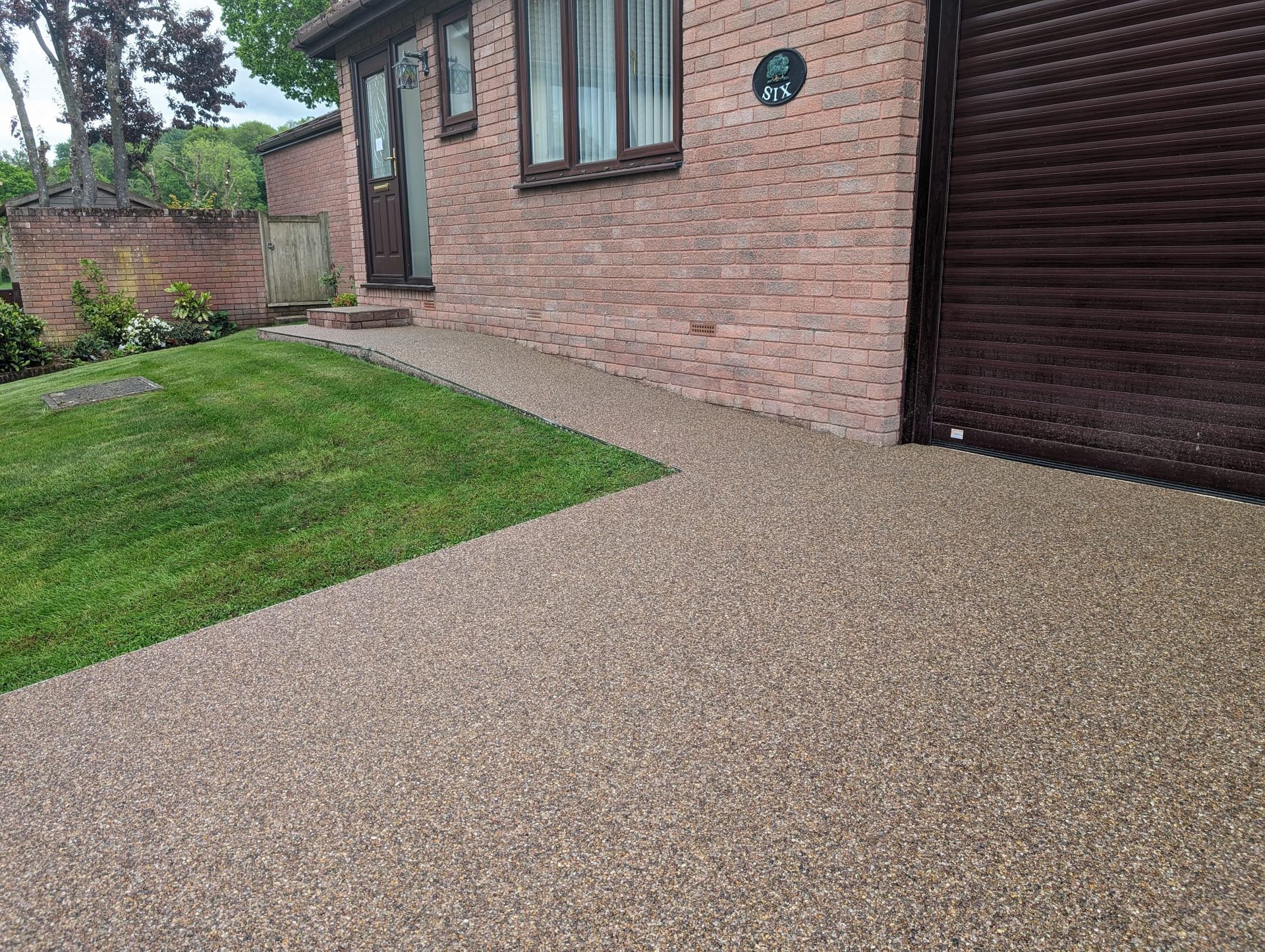 Brown resin driveway in front of a red house, with green grass on the side.