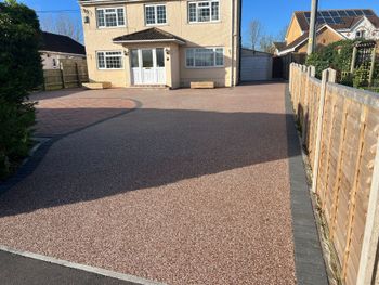 Red resin driveway leading up to a beige two story house