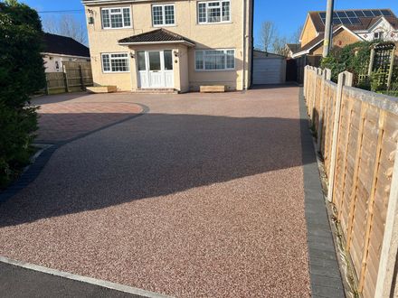 Red resin driveway leading up to bege two story house